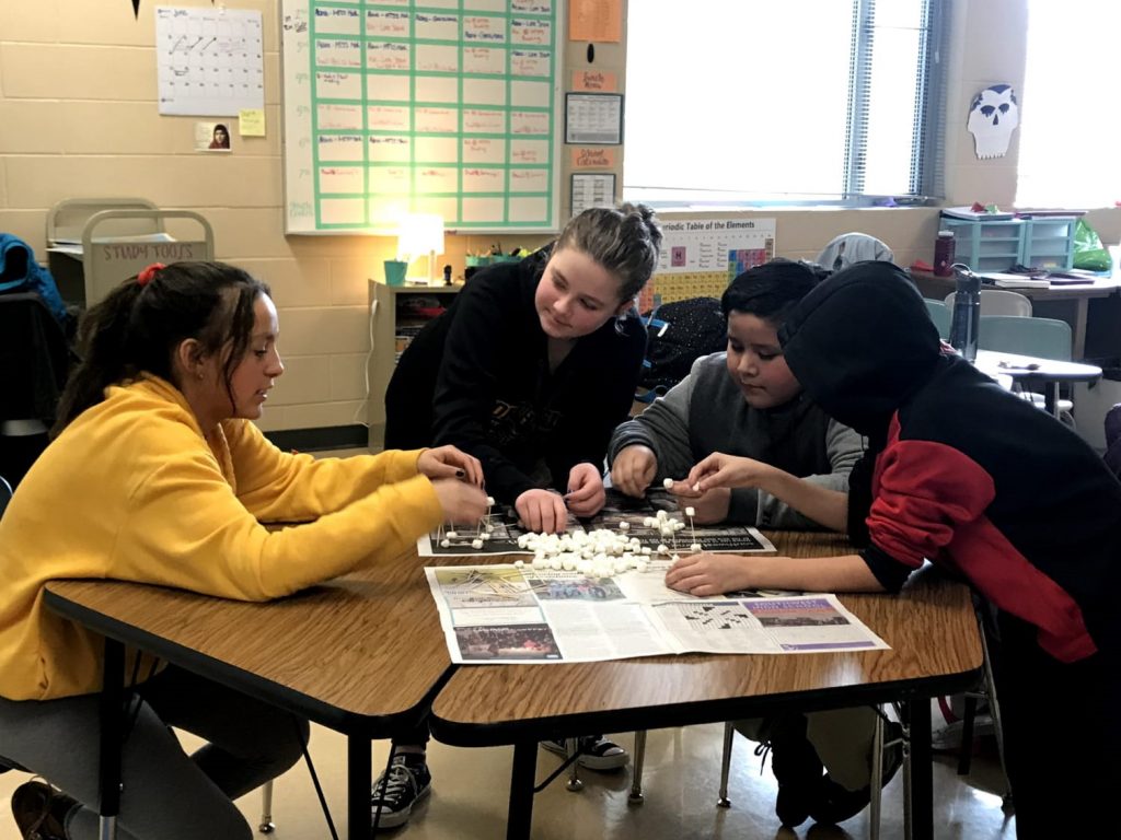 St. Olaf student demonstrates an activity to three middle school youth at a table.