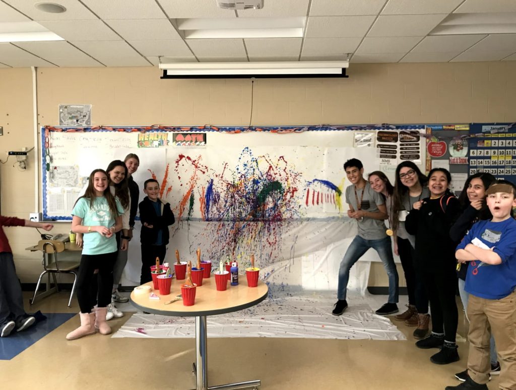 Group of middle school youth stand in front of splatter painting