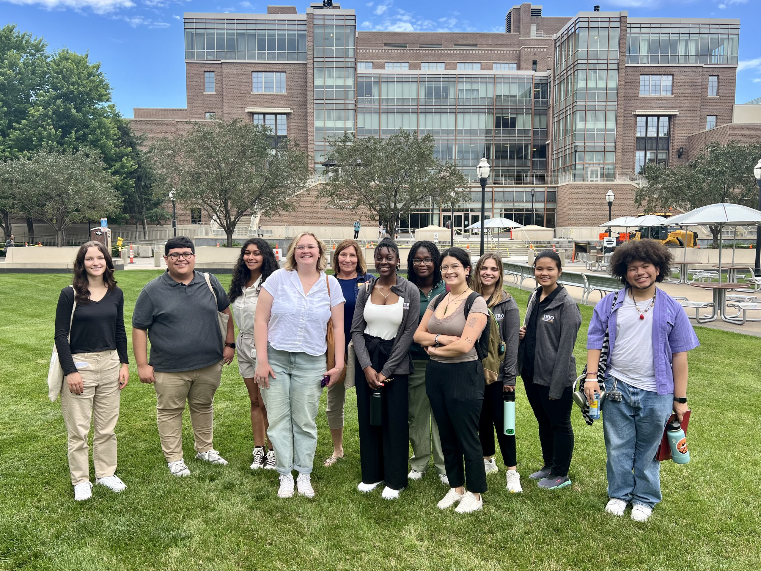 10 TRIO McNair Summer 2024 researchers visiting the UMN Twin Cities campus, standing on grassy area in behind Coffman Union building.