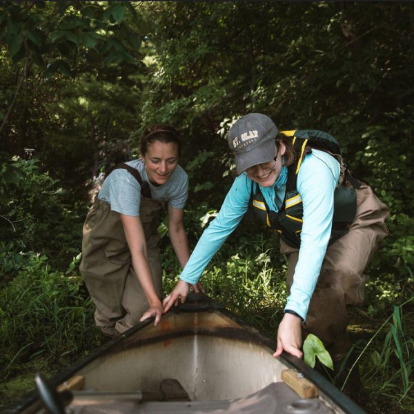 Two students in waders pushing a kayak